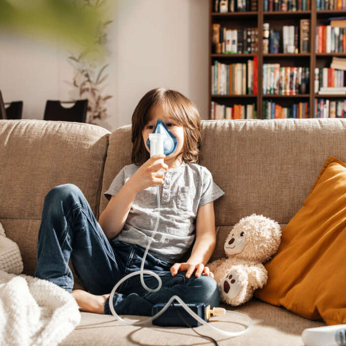 A little boy makes an inhalation at home sitting on the couch using a nebulizer and a mask. Prevention of lung diseases. home treatment. A little boy makes an inhalation at home sitting on the couch using a nebulizer and a mask. Prevention of lung diseases. home treatment